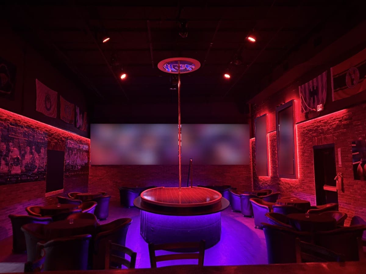 The main stage at Knockouts Houston: a round stage with a single pole, lit purple from below and ringed by tub chairs, in front of a wide video wall